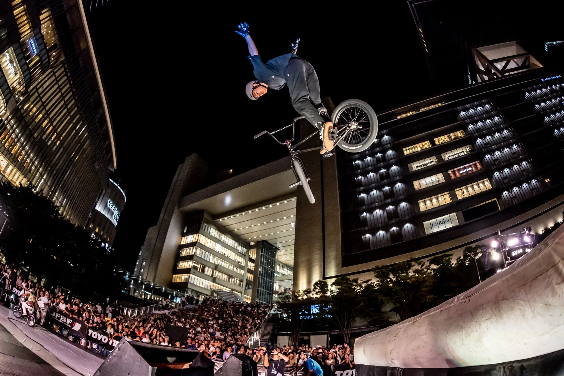 夜の都市を背景に、BMXライダーが観客の前でダイナミックなジャンプトリックを披露