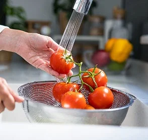 キッチンで、蛇口から流れる水を使って新鮮なトマトを洗っている場面
