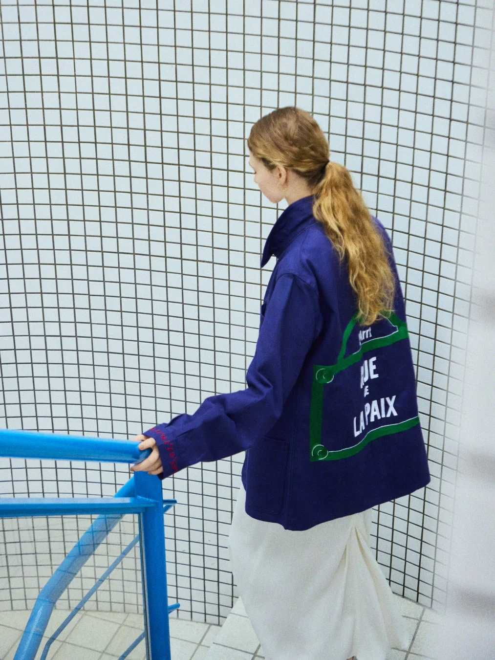 ネイビーのジャケットを着た女性が階段を降りている様子、背面に「RUE DE LA PAIX」の文字