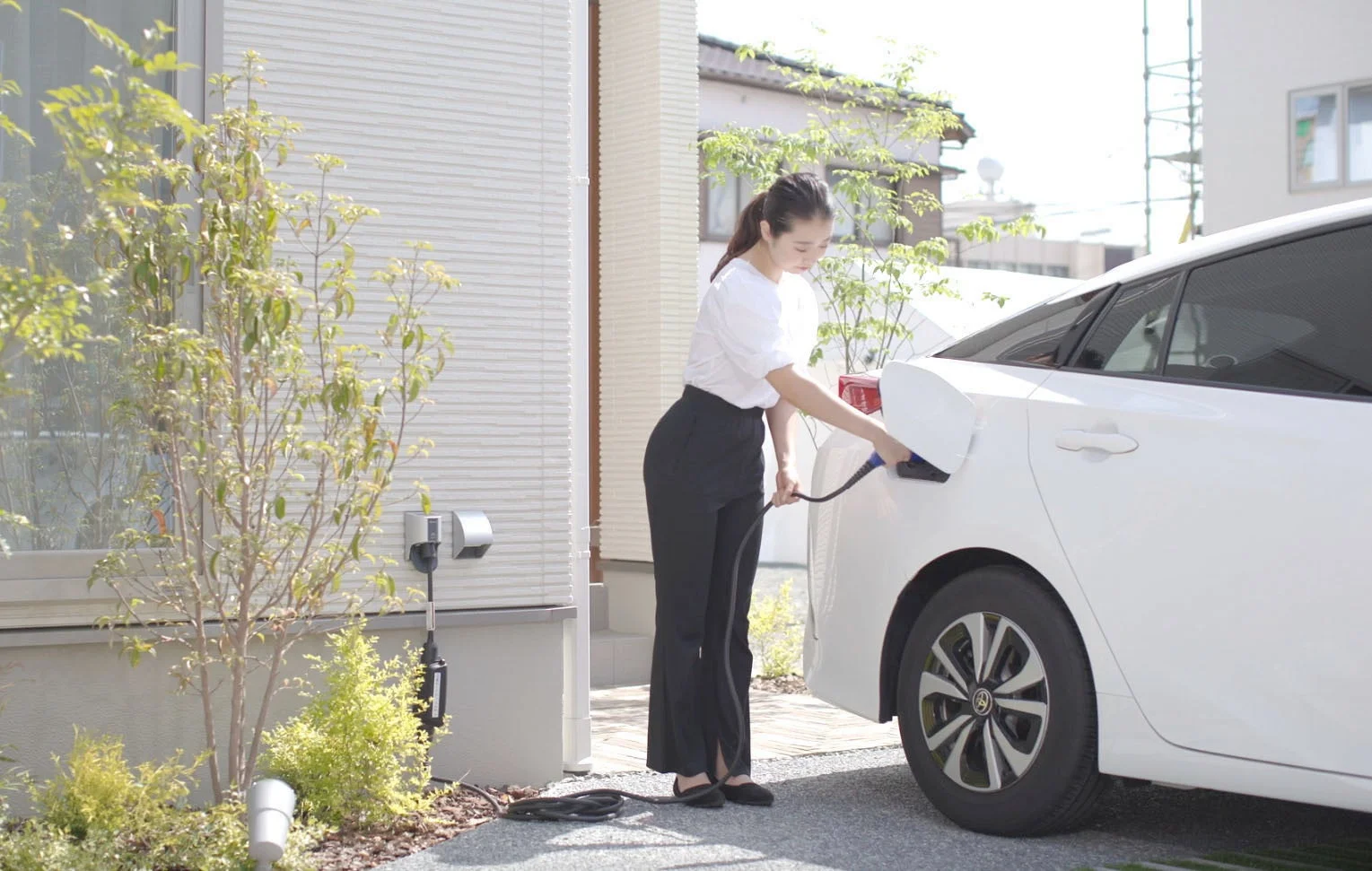 自宅の充電ステーションで電気自動車に充電している女性