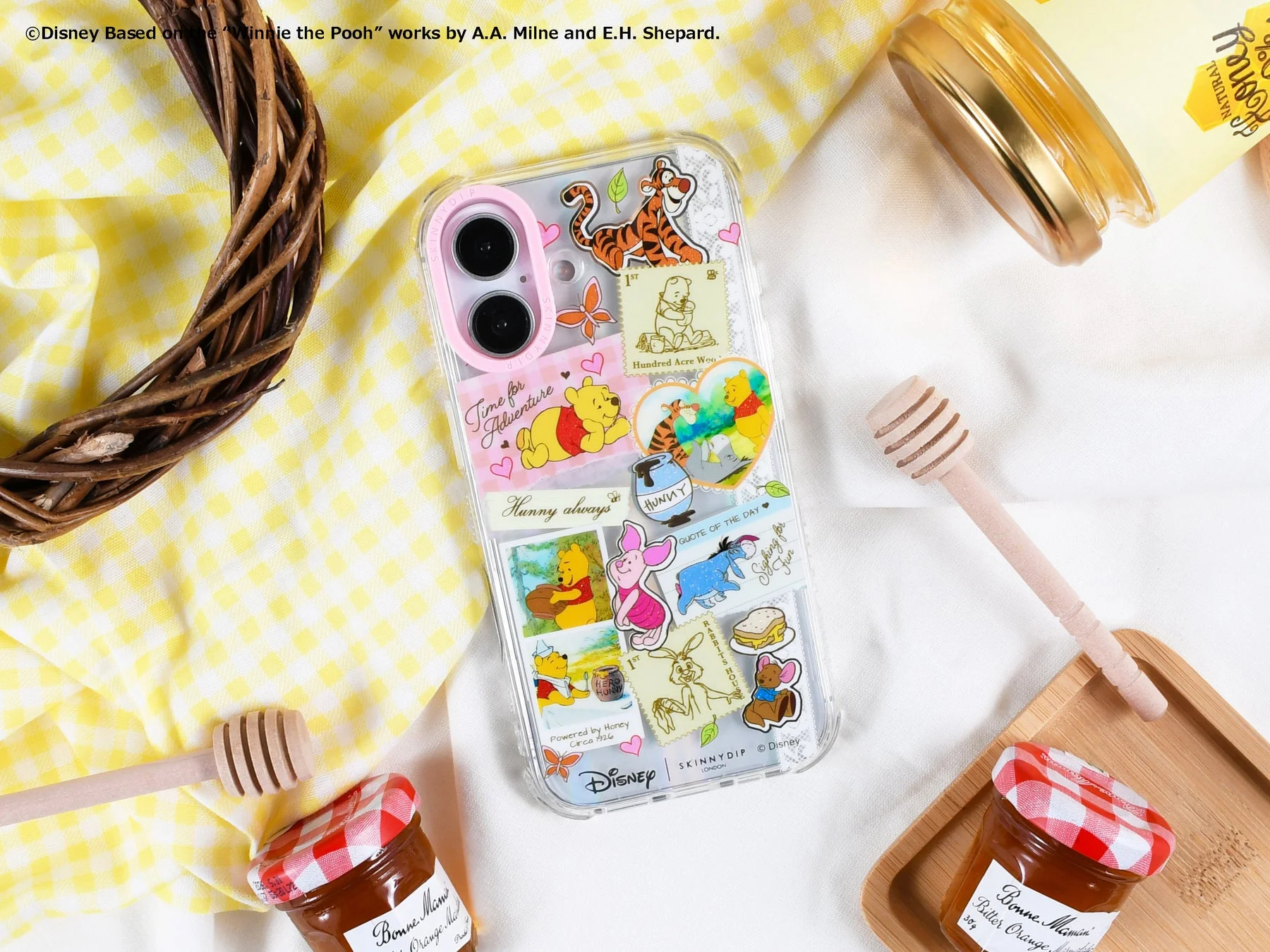 くまのプーさんのキャラクターがデザインされたスマートフォンケースを中心に、ハチミツやジャム、ハニーディッパーが並べられた可愛らしい写真