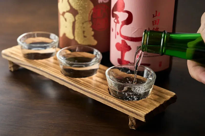 緑色の瓶から小さなガラスの器に注がれる日本酒