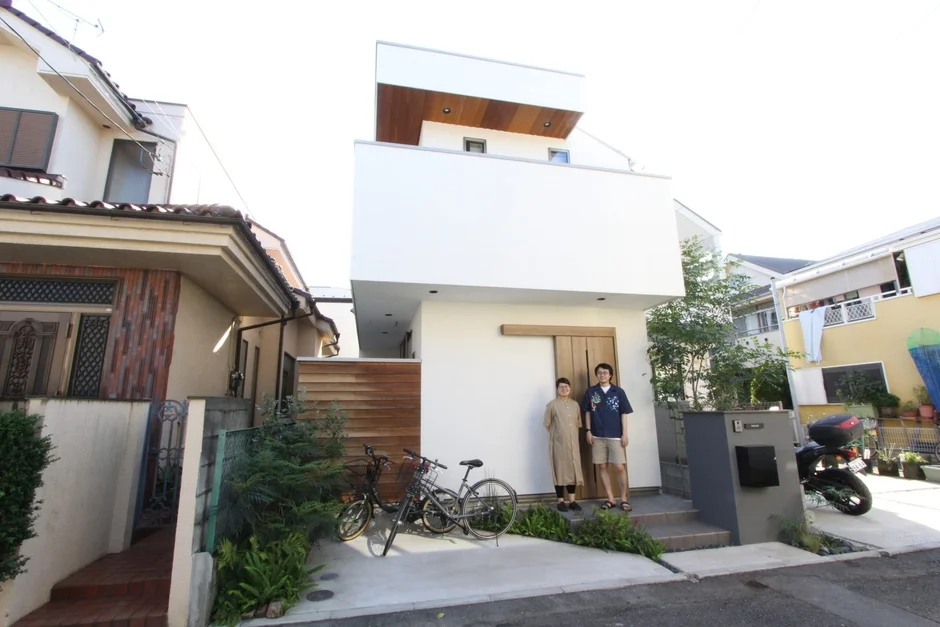 白いモダンな外観の住宅の前に立つ夫婦