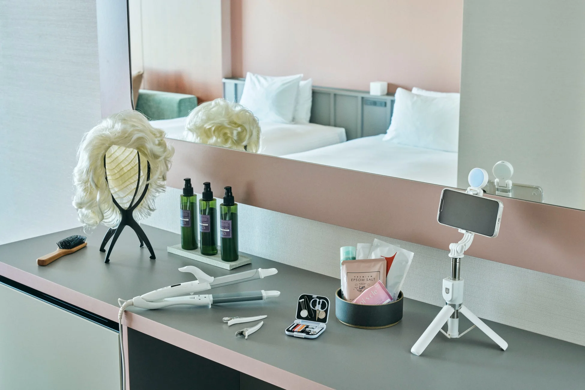 ホテルの客室にあるドレッサーに、ウィッグ、ヘアアイロン、ボトル入りの美容液、入浴剤、スマートフォン用三脚など、美容やセルフケア、Vlog撮影に使えるアイテムが並べられています。快適な滞在をサポートする充実した設備が伺えます。