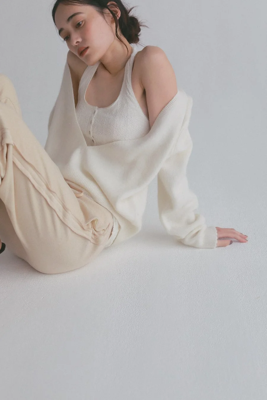 オフホワイトとベージュのカジュアルな服装で座る女性