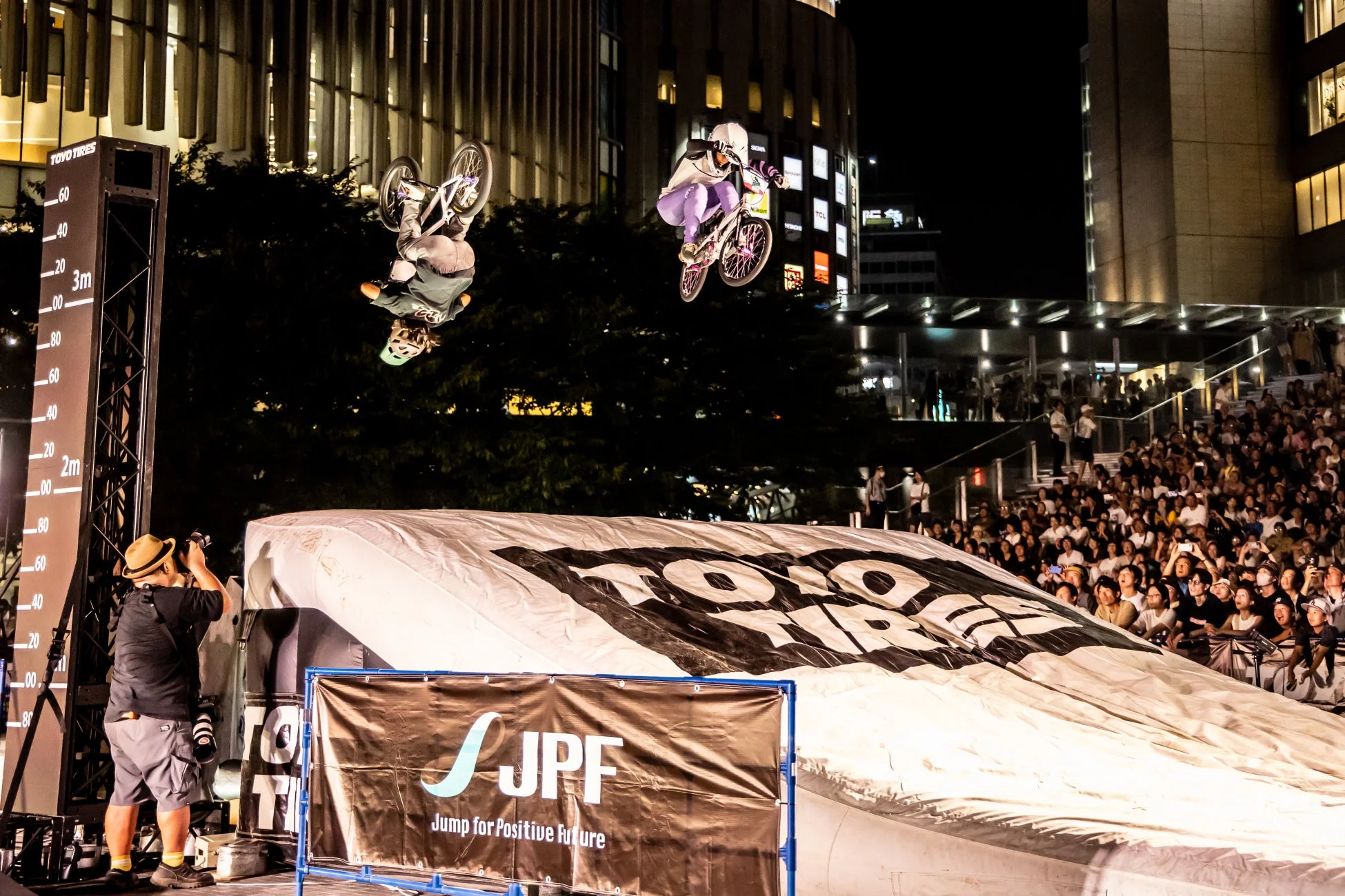 夜の都市で開催されたBMXイベントで、2人のライダーが空中でダイナミックなトリックを披露