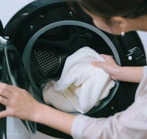 女性がドラム式洗濯機に白いタオルを入れている場面