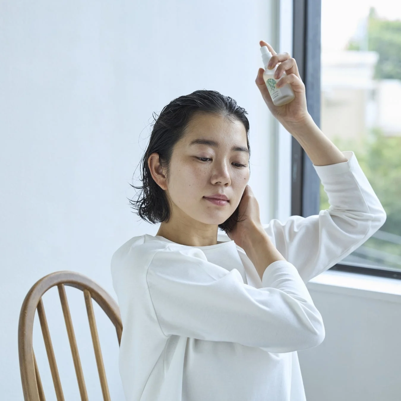 ウェットヘアの若い女性が白いスプレーボトルを使って髪に製品を塗布している様子です。