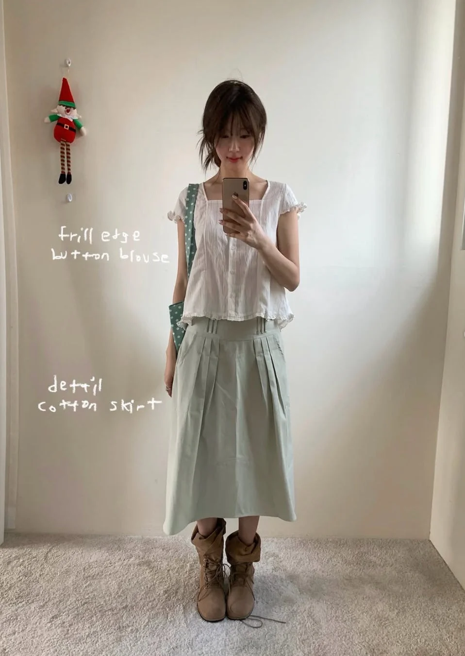白いフリルブラウスとミントグリーンのプリーツスカートを着用した女性が、ミラー越しに自撮り