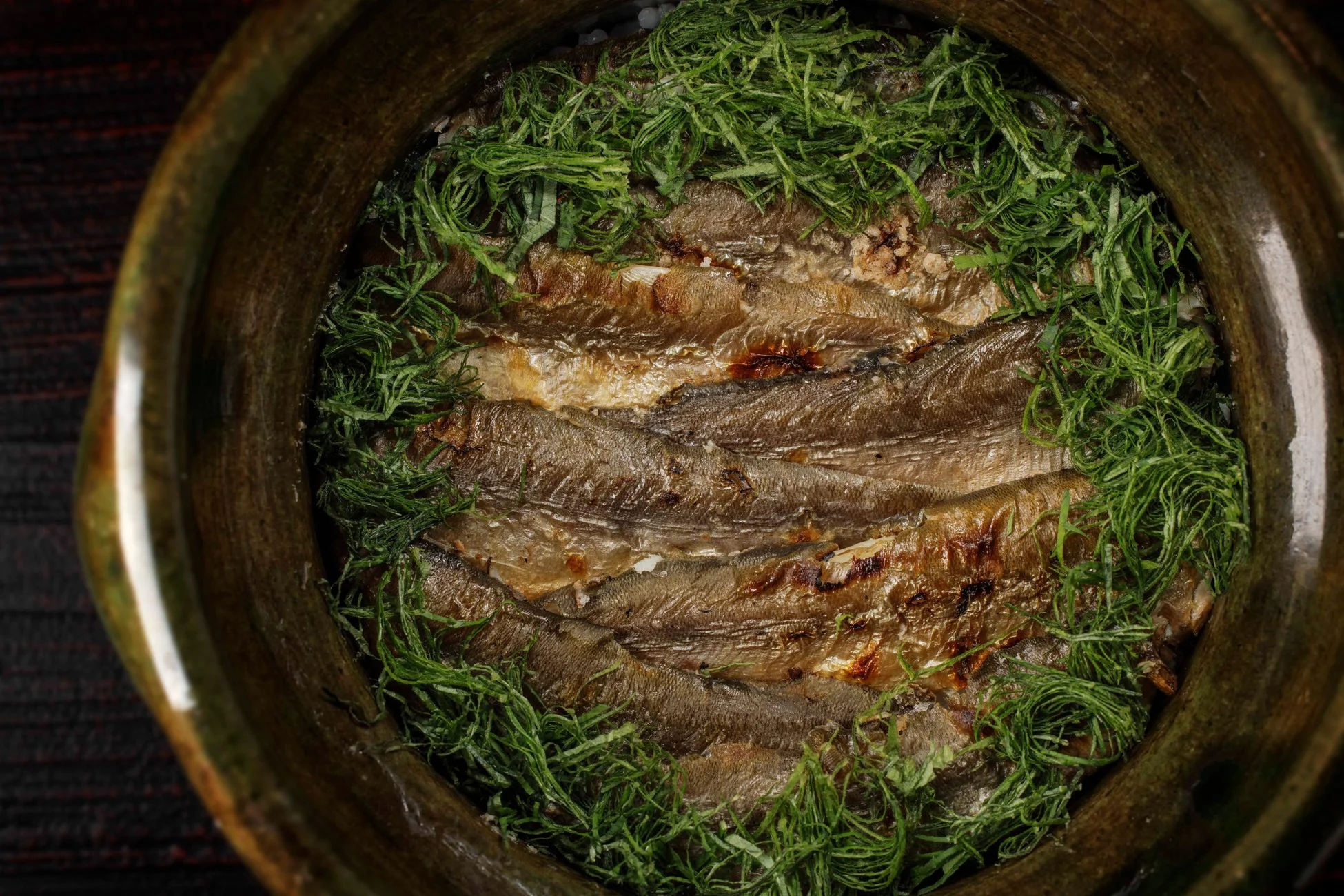 土鍋に入った小魚の焼き魚で、緑豊かなハーブが添えられています