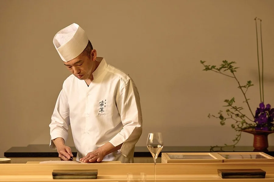 白い調理着を着た日本の職人が、洗練された雰囲気のカウンターで食材を丁寧に準備している様子