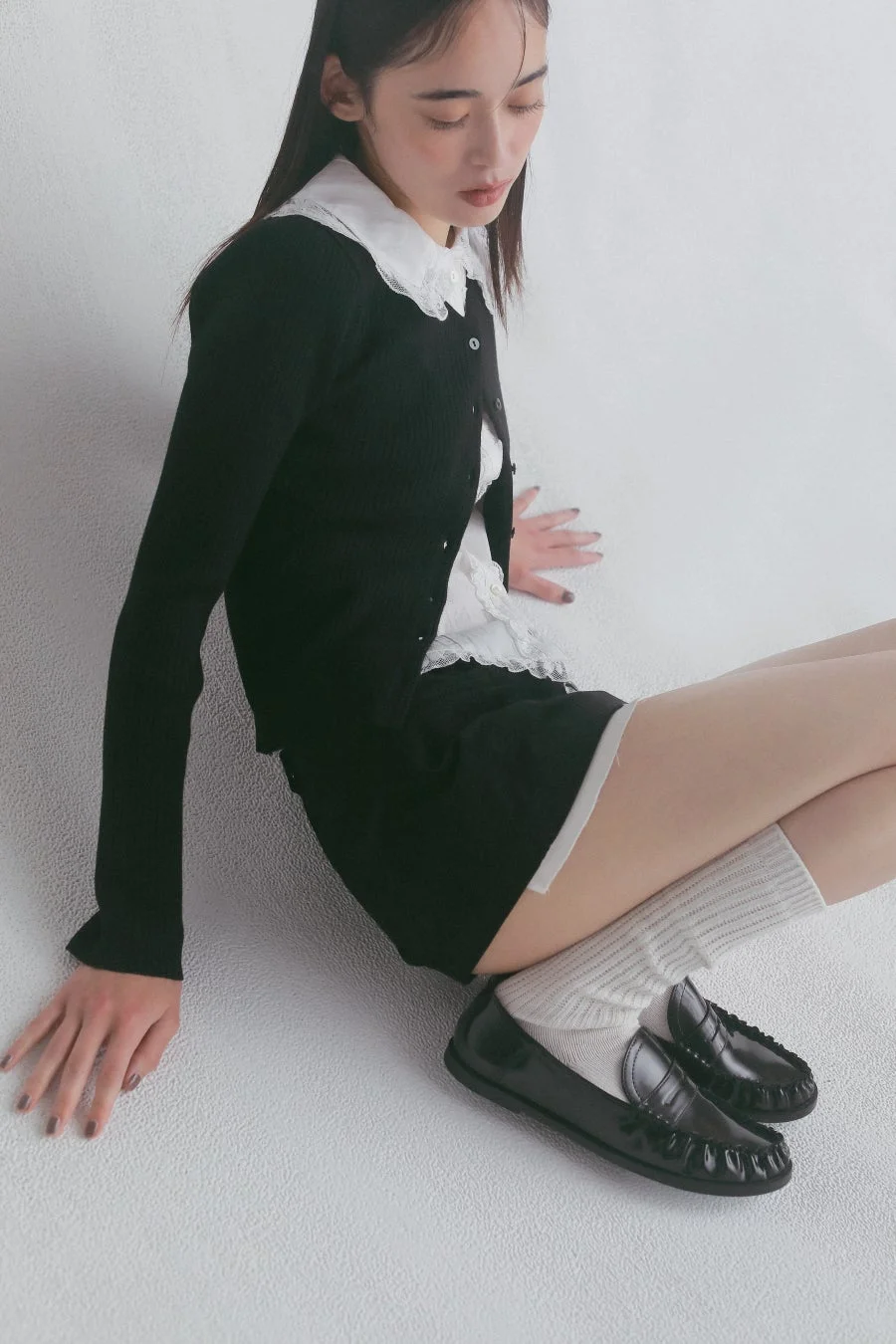 黒いカーディガンと白い襟のシャツ、ショートパンツを着用し座る女性