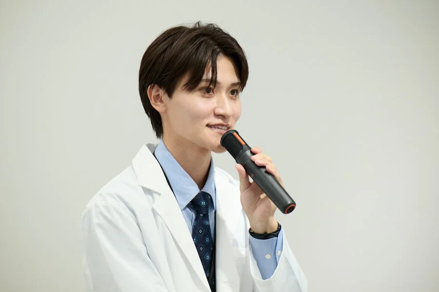 白衣を着た男性がマイクで話す様子