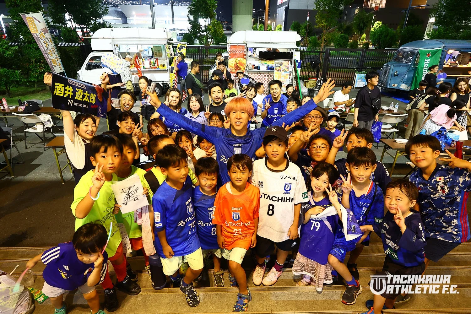 屋外イベントでサッカーユニフォームを着た子供と大人の集合写真