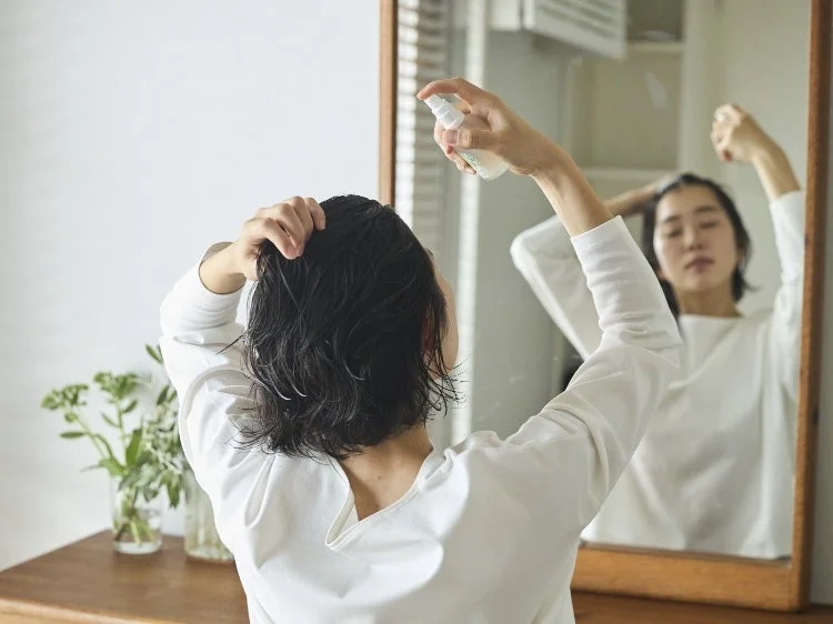 ウェットヘアの女性が鏡に向かってヘアスプレーを使用しています。