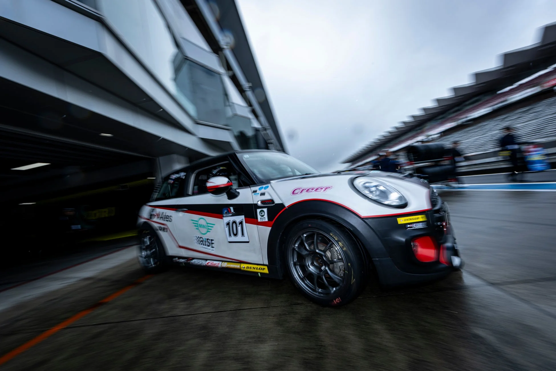 雨上がりのサーキットを走るMINIのレーシングカー「101号車」が写っています