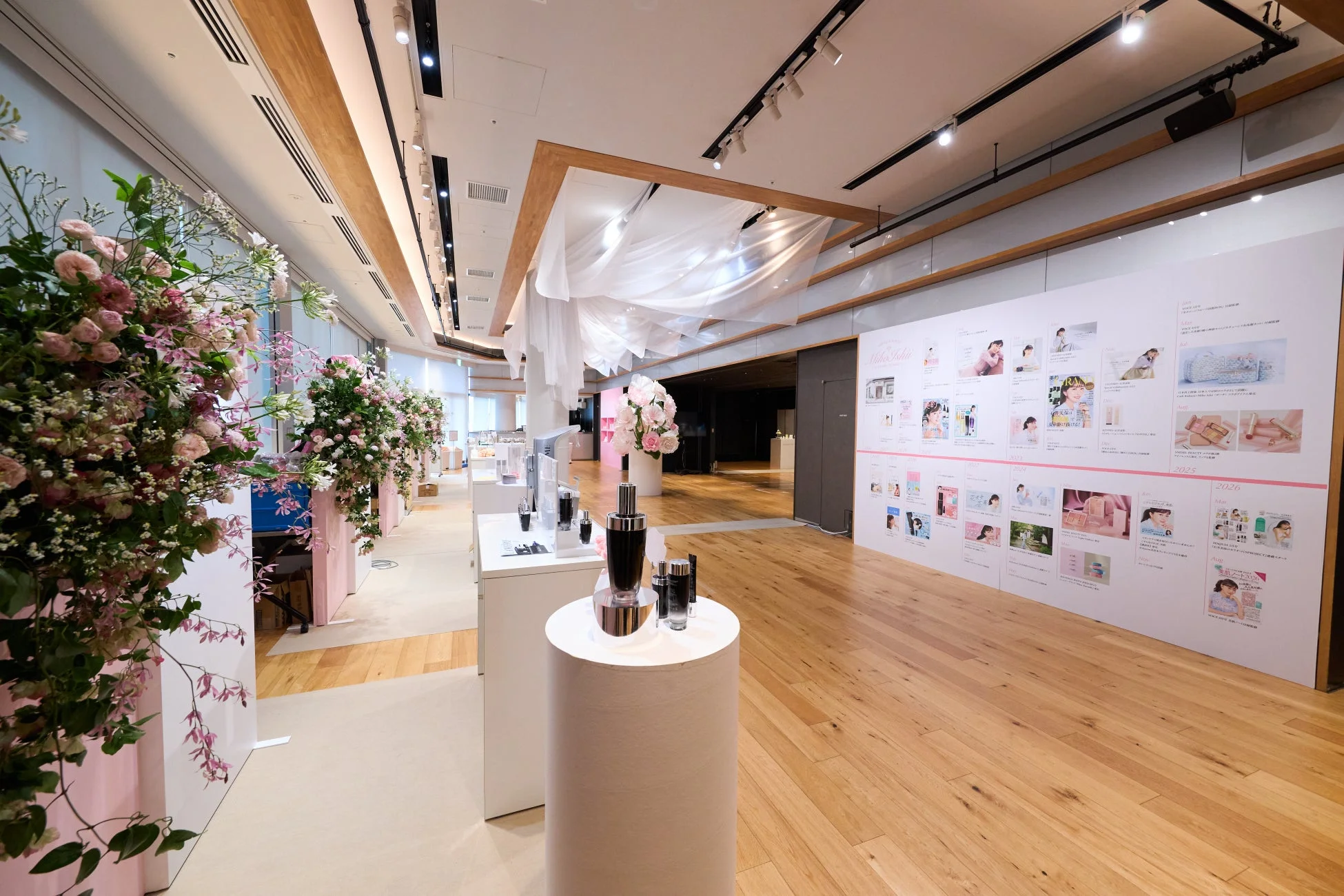 ピンクと白の花で飾られた広々としたイベントスペースで、化粧品やスキンケア製品が展示されています。