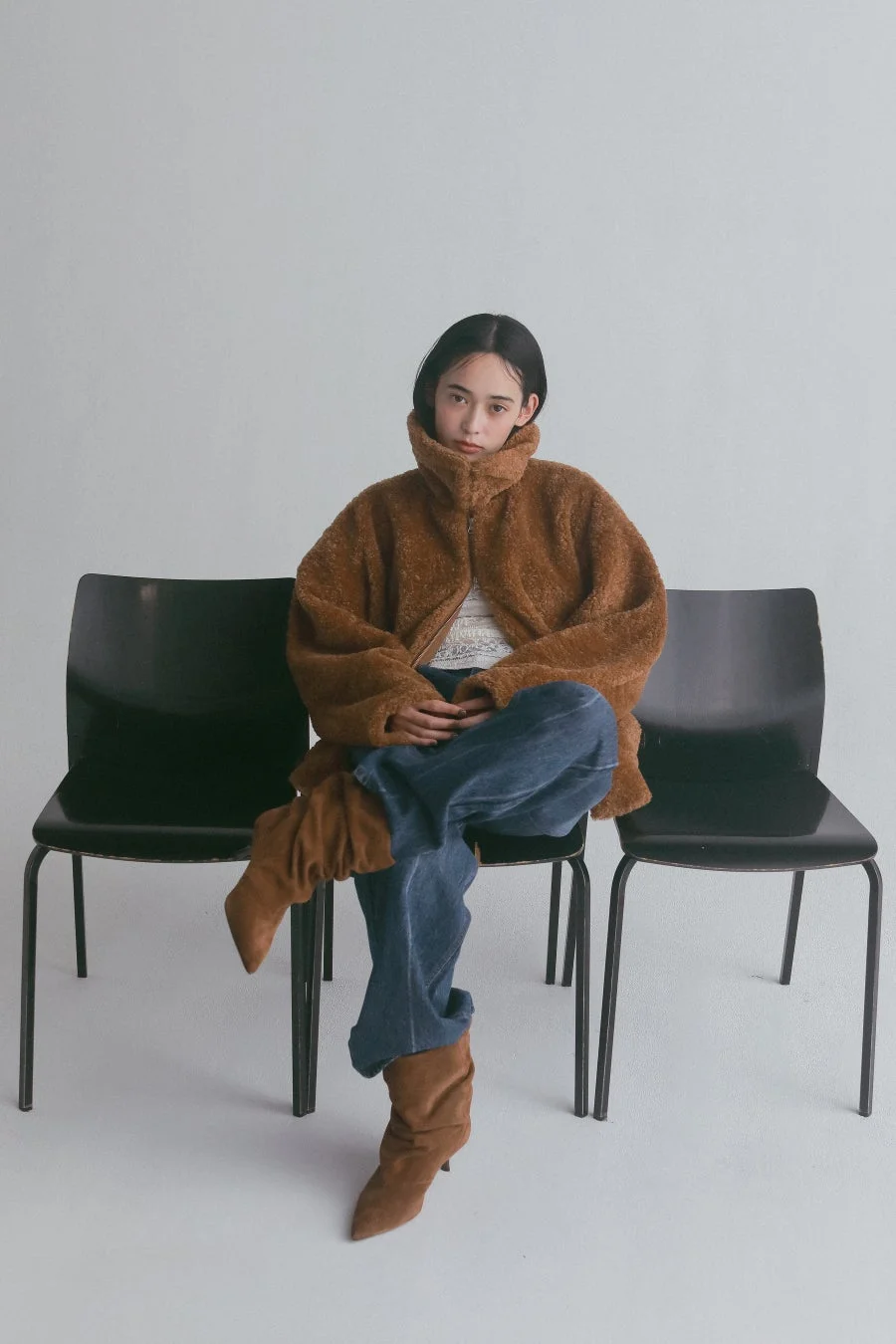 茶色のボアジャケットとジーンズ、茶色のブーツを着用し椅子に座る女性