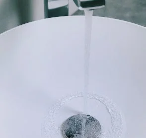 蛇口から白いシンクに水が勢いよく流れ落ち、排水口の周りに波紋が広がる様子