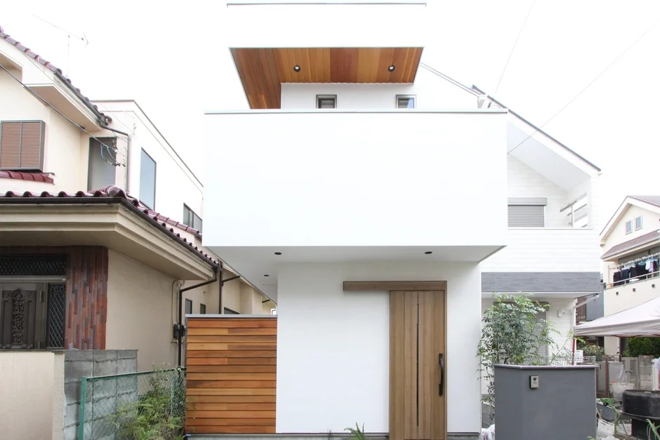 白い外壁と木製ドアが特徴のモダンな戸建て住宅