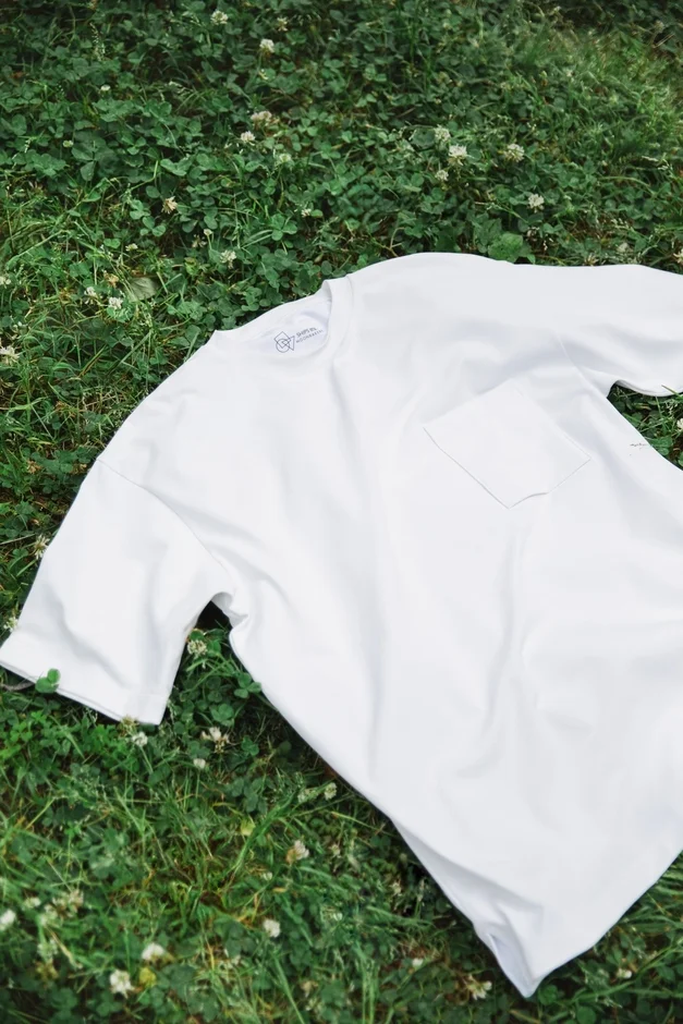白い無地のTシャツが、緑豊かな芝生の上に広げられている様子を捉えた画像です。