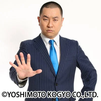 ダークスーツと青いネクタイを着用した男性が、真剣な表情で片手を上げて「停止」や「拒否」を示すジェスチャーをしている画像