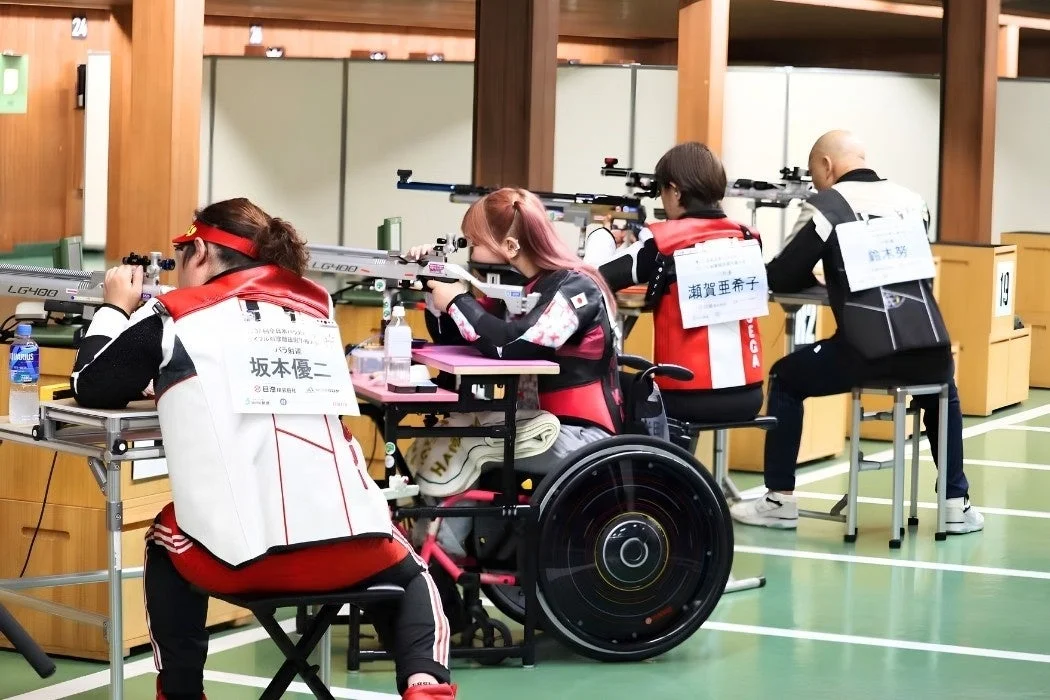 屋内の射撃場で車椅子のアスリートがライフルを構えている画像