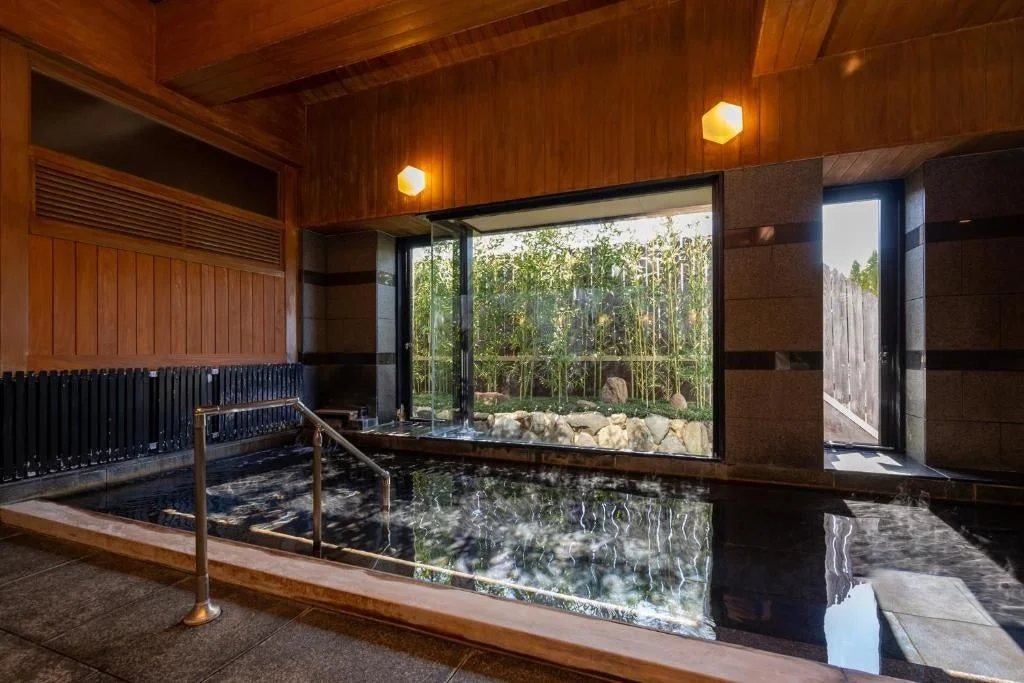 和風の落ち着いた雰囲気の屋内浴場です。大きな窓からは手入れされた竹林の庭園が望め、湯船に浸かりながら自然を感じられます。木材を基調とした内装が心地よいリラックス空間を演出しています。