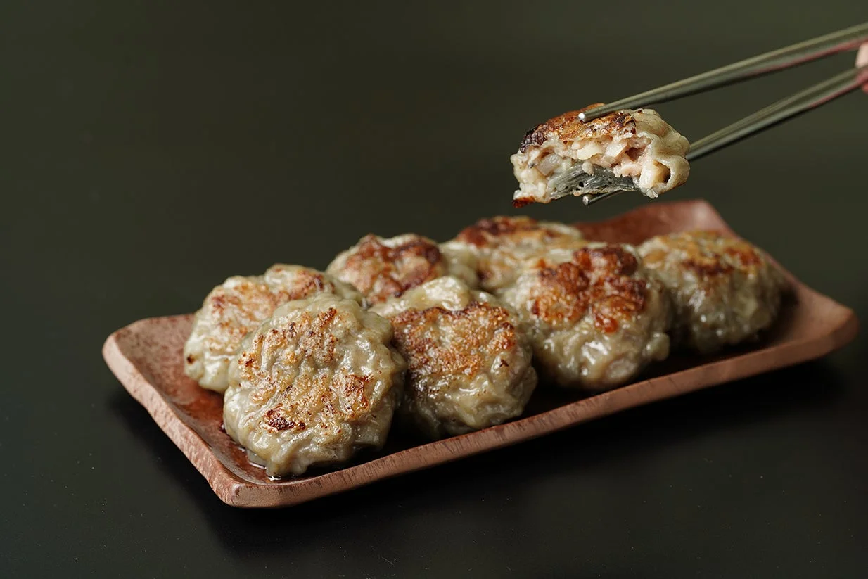 焦げ目が香ばしい焼き餃子が皿に盛られ、一つが箸で持ち上げられています