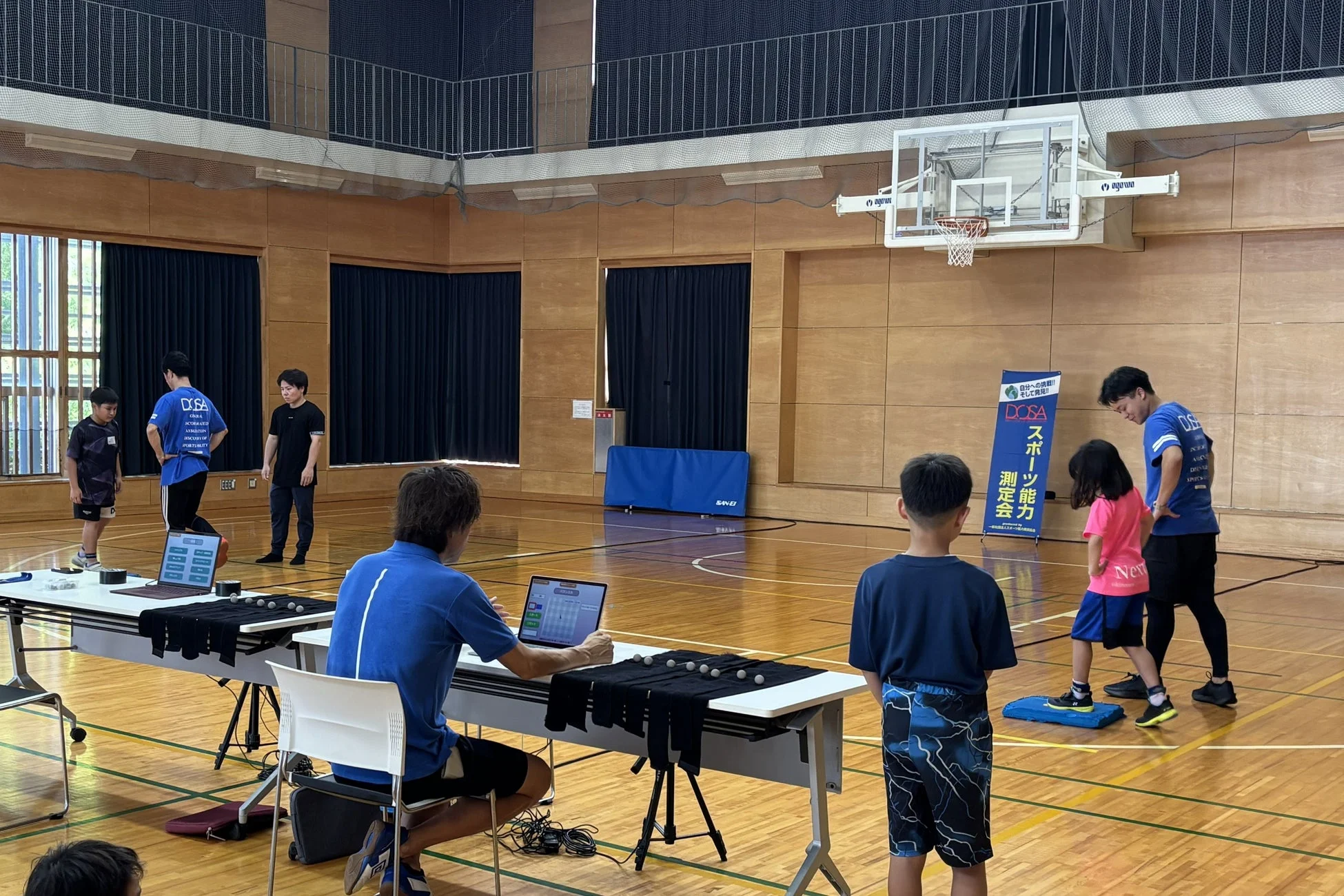 体育館でDCSAによるスポーツ能力測定会が開催されている。子供たちが指導者のもとで運動能力を測定