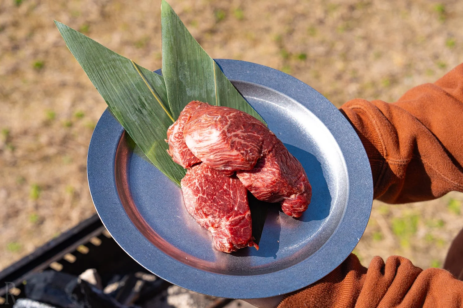 屋外で、新鮮な霜降りの牛肉の塊が笹の葉を敷いた銀色の皿に盛られています