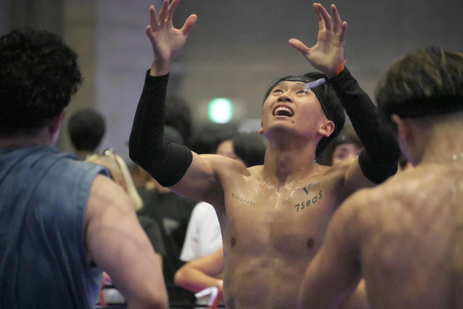 汗をかいた男性が両手を高く掲げ、天を仰ぎながら喜びや達成感を表現しています。イベント会場のような場所で、感情的な瞬間を捉えた一枚です。