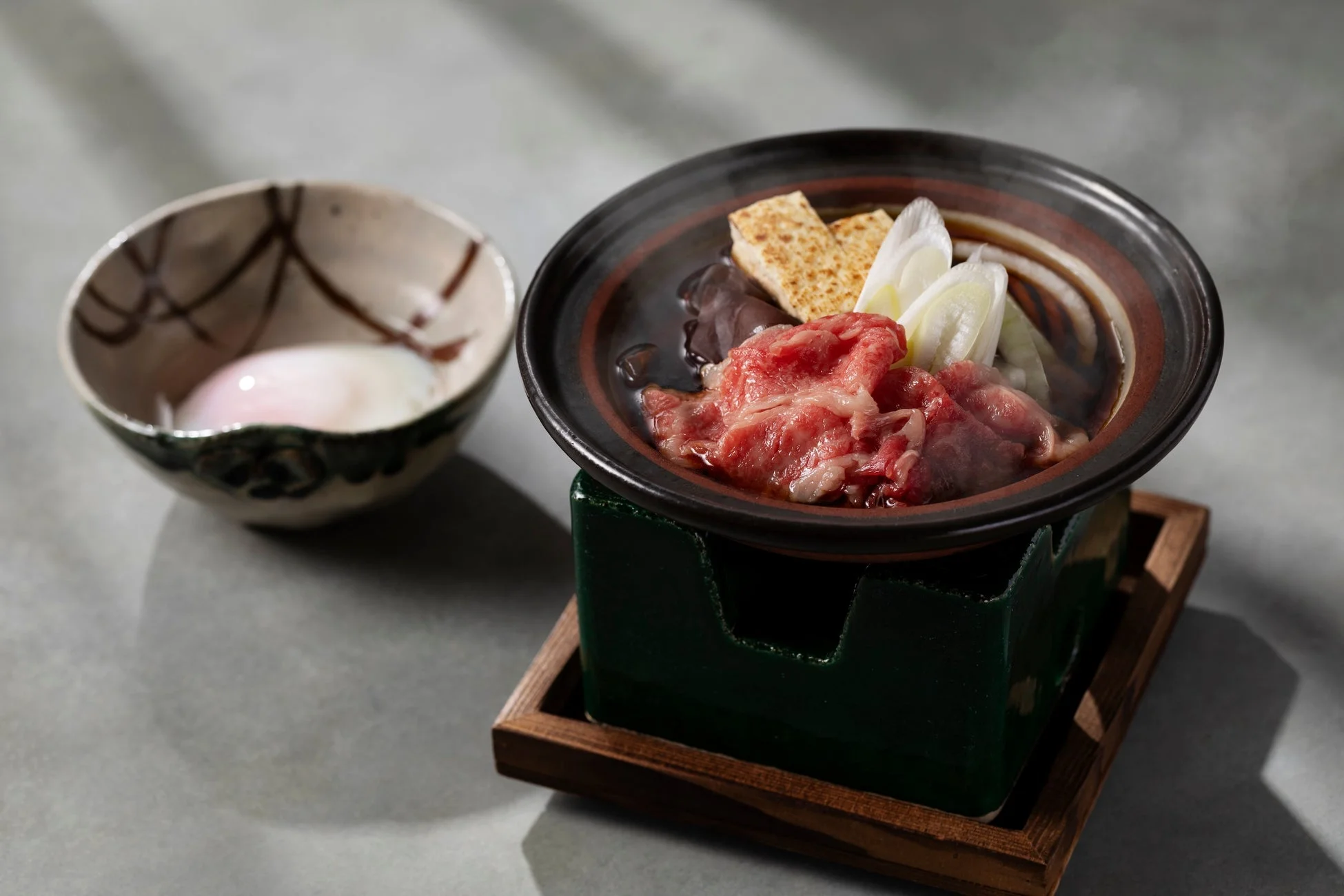 熱々のすき焼き鍋が食卓に置かれ、新鮮な牛肉、豆腐、長ネギが盛り付けられています