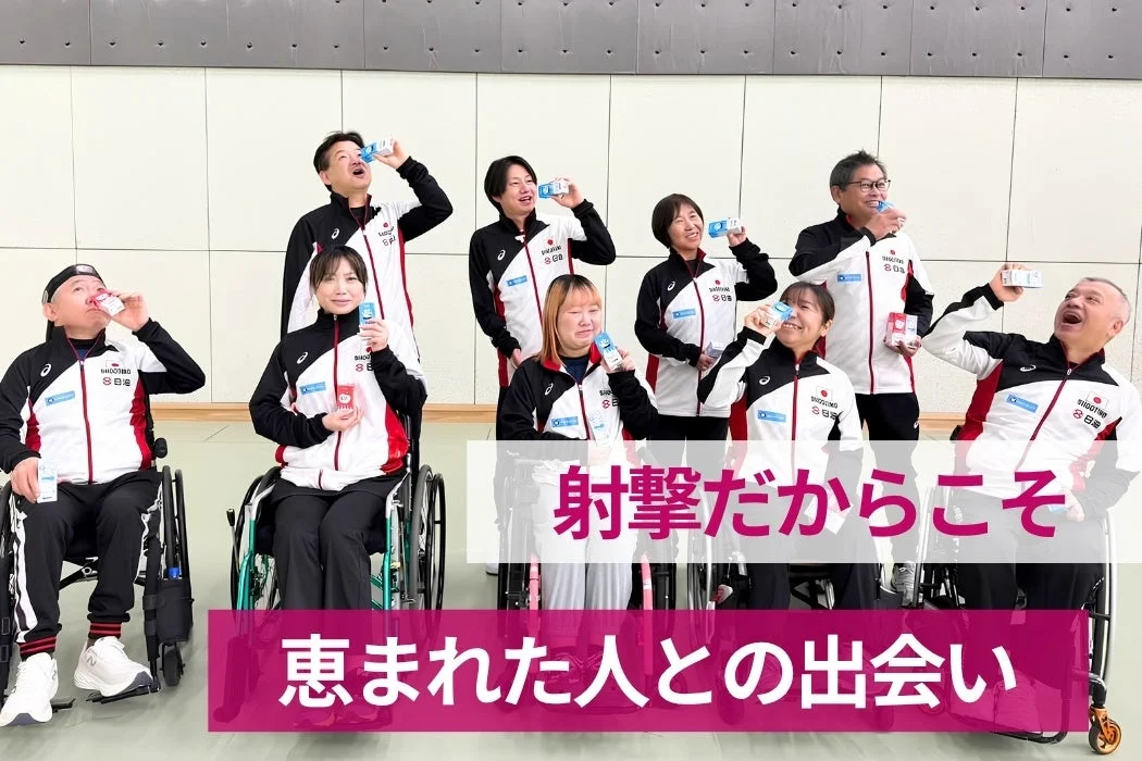 車椅子に乗っている人も含め、数人の人々がアスリートウェアを着用し、笑顔で飲料を飲んでいる集合写真