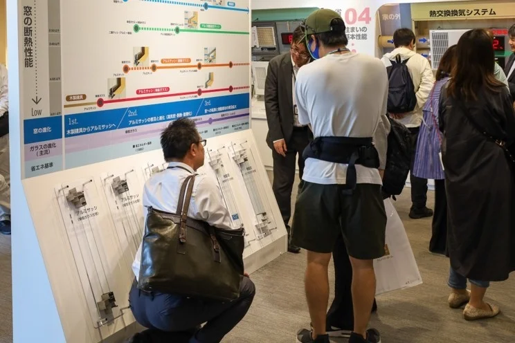 窓の断熱性能やサッシの進化に関する展示パネルと実物サンプルを見学する来場者