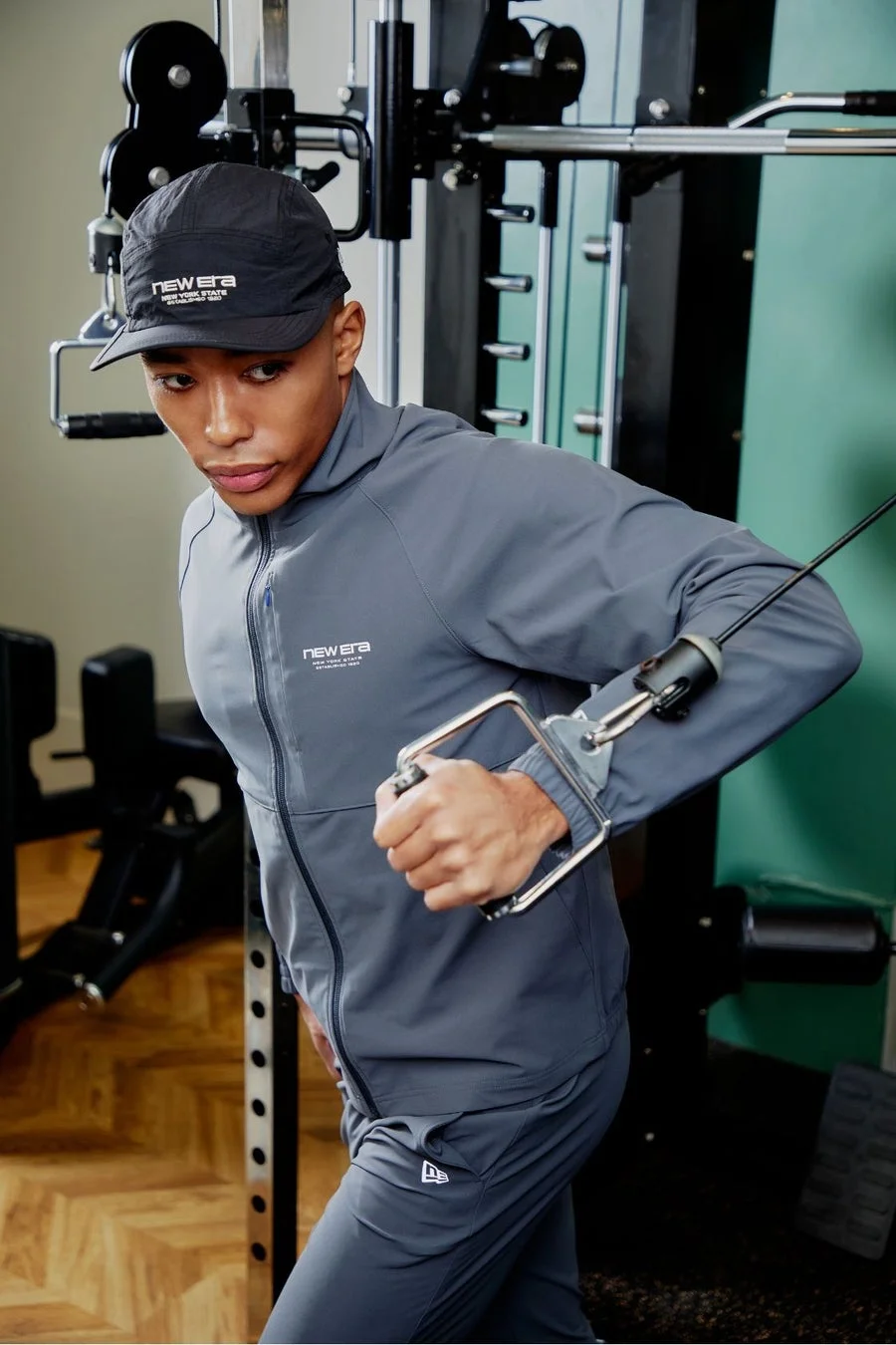 NEW ERAのスポーツウェアを着用した男性が、ジムでケーブルマシンを使ってトレーニングをしている様子