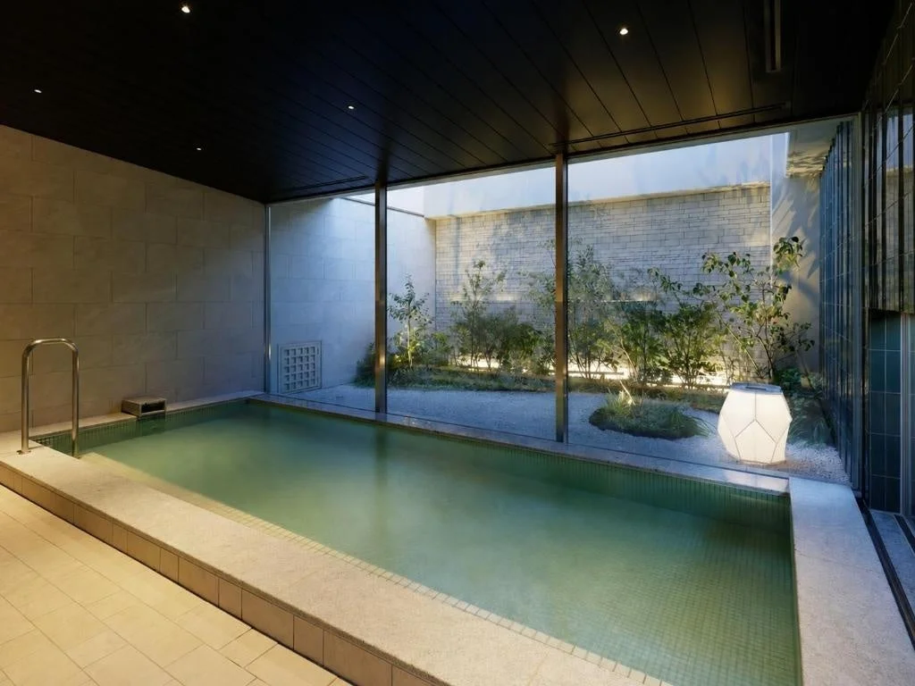 窓越しに緑豊かな坪庭が見えるモダンな屋内プール（または浴場）。落ち着いた雰囲気でリラックスできる空間です。