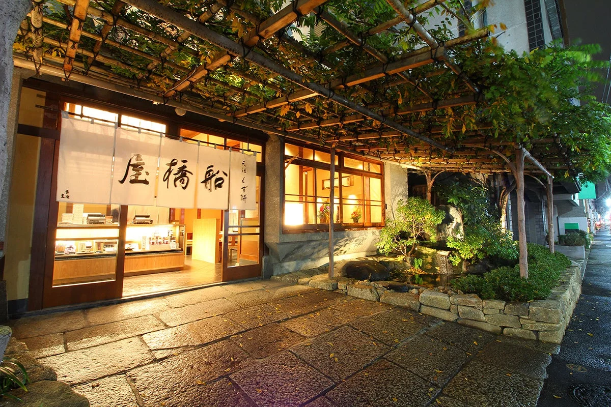 夜の日本家屋の入り口に暖簾がかかる船橋屋本店の外観