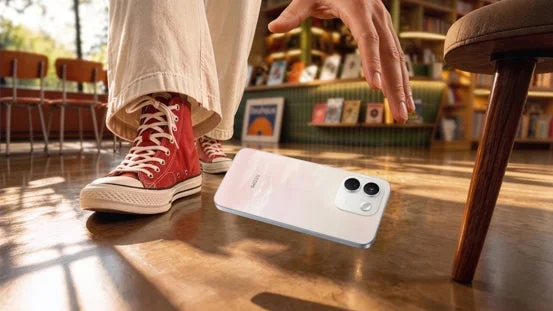 赤いハイカットスニーカーとワイドパンツを履いた人物が、木製の床に置かれた白いスマートフォンに手を伸ばしている
