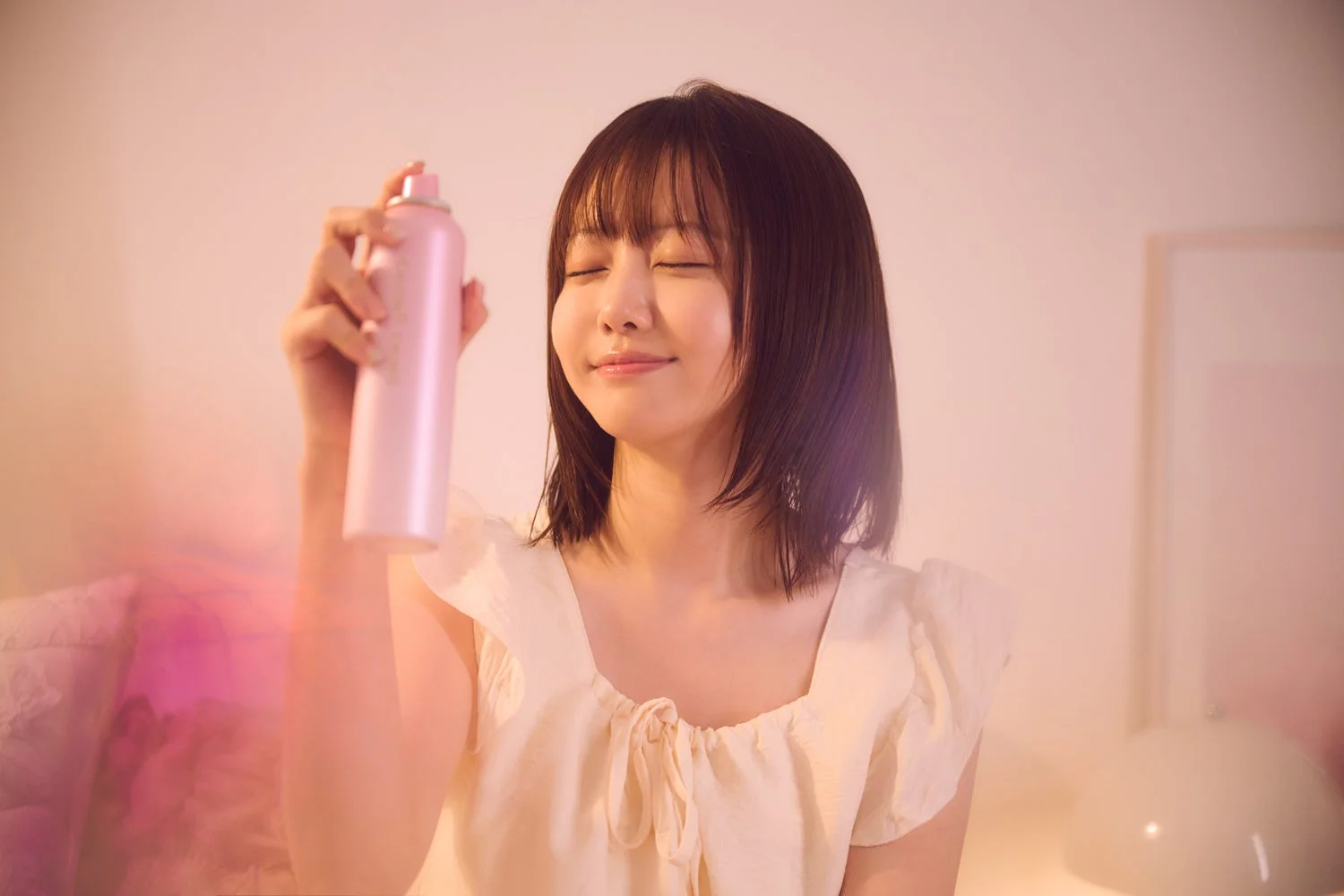 若手女性が目を閉じて顔にピンク色のスプレーをかけている様子