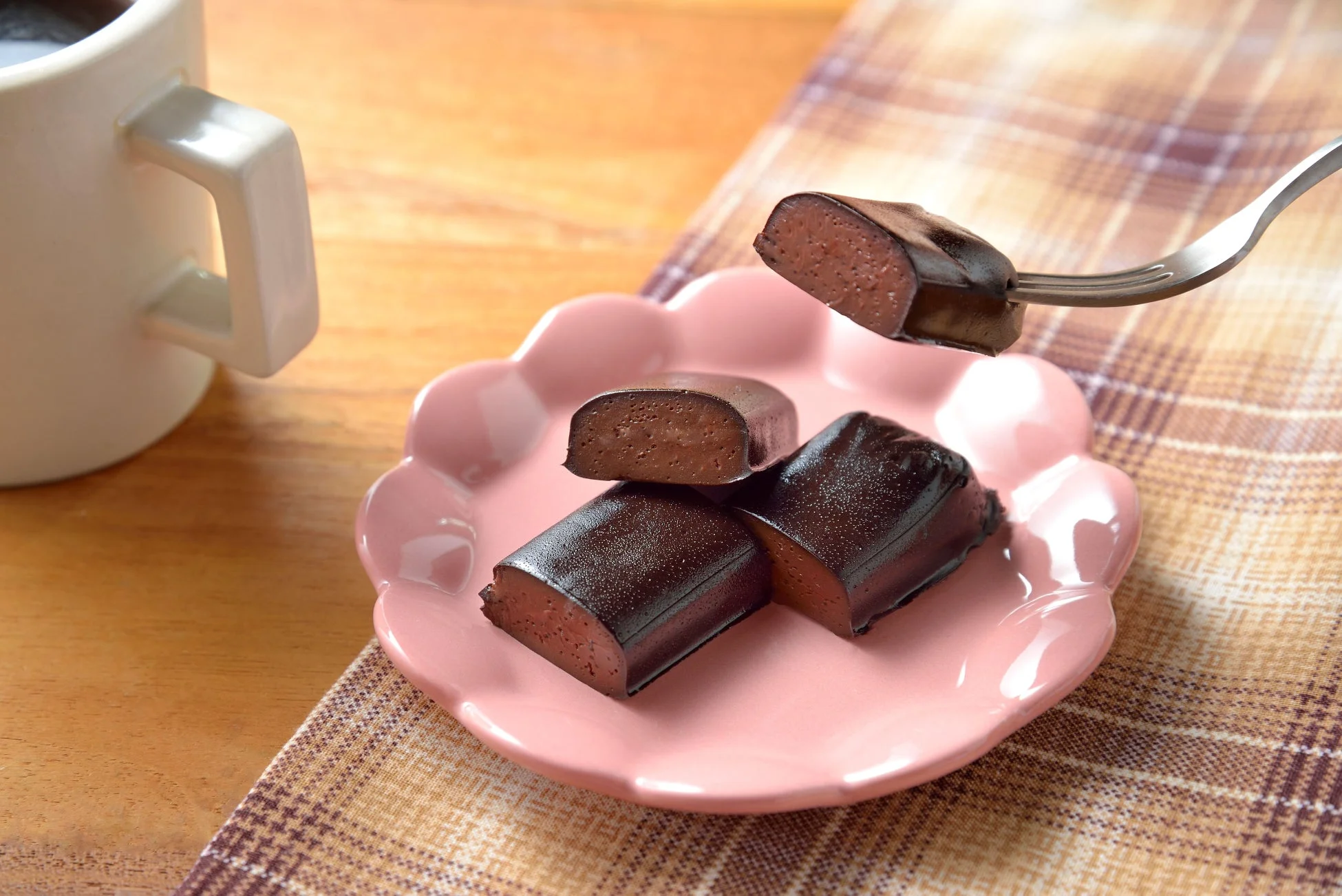 ピンクの皿に盛られたチョコレート色のスイーツをフォークでつまんでいる様子