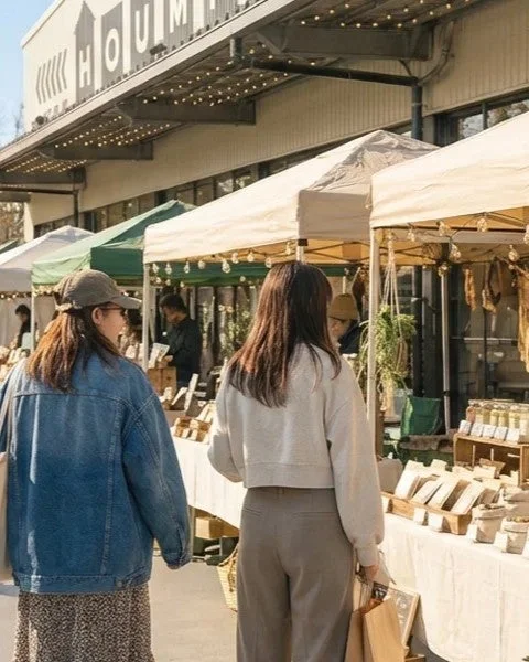 晴れた日に屋外マーケットを訪れる二人の女性が写っています。