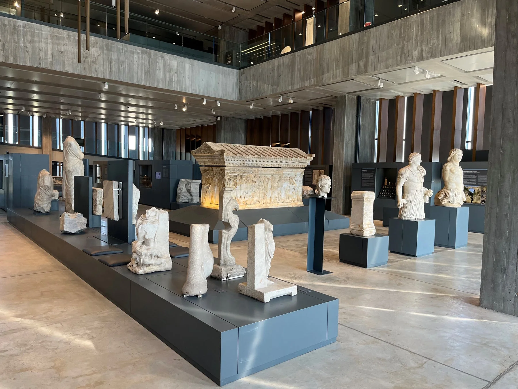現代的な博物館の展示室で古代の石像や石棺が展示されている
