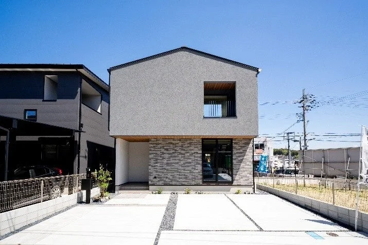 グレーの壁とレンガ調のサイディングが特徴的なモダンな二階建て住宅