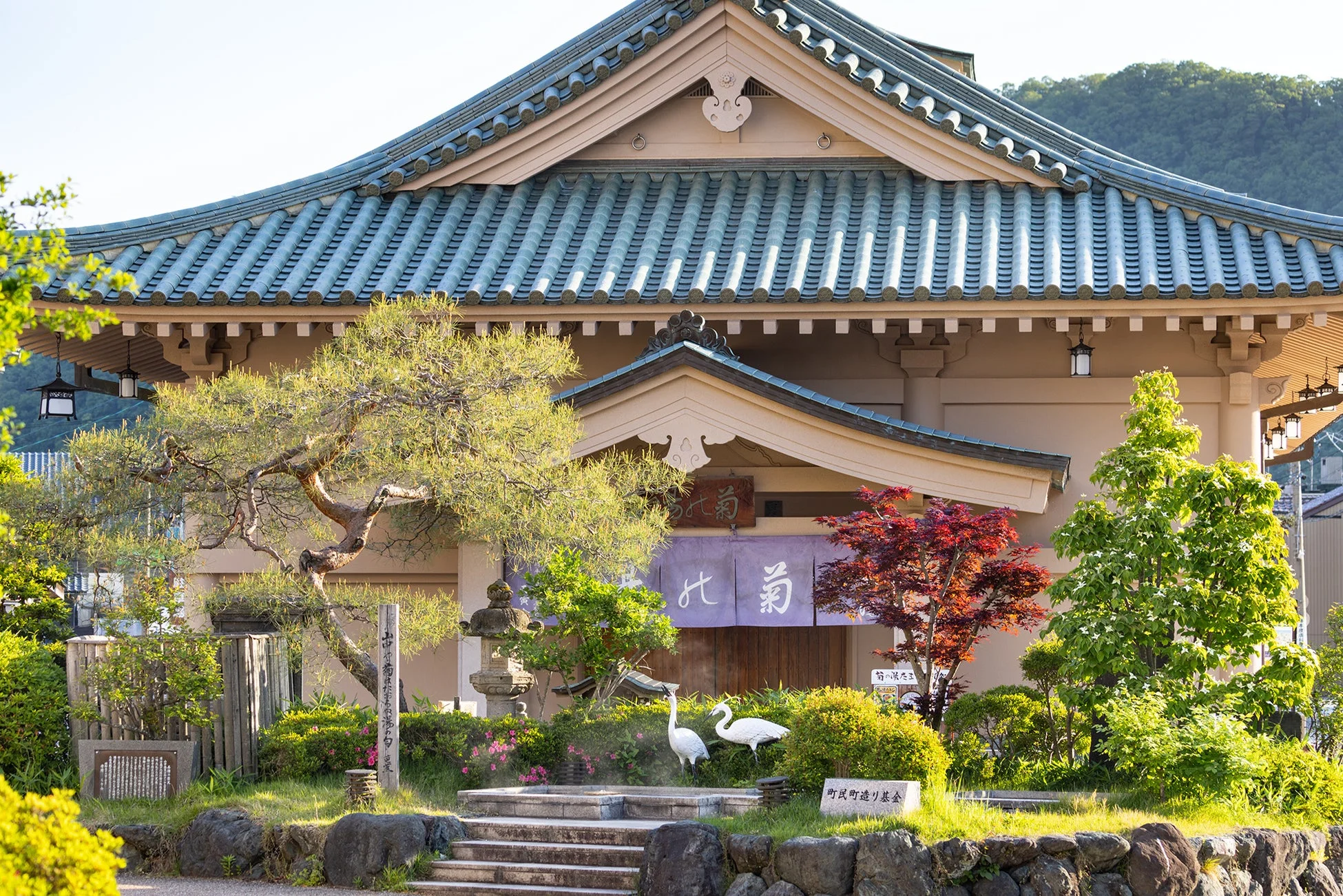 青い瓦屋根の伝統的な日本建築と、手入れされた日本庭園の風景。