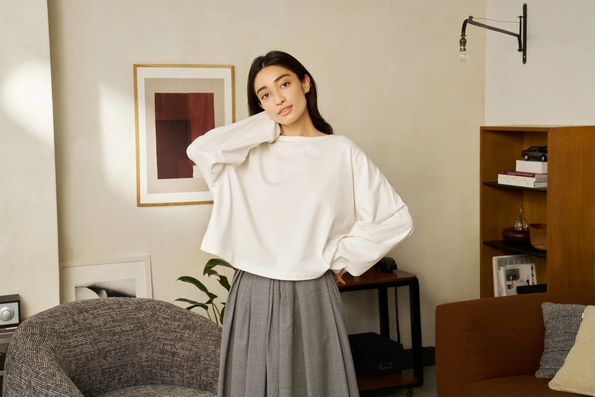 白い長袖トップスと千鳥格子のプリーツスカートを着用した女性