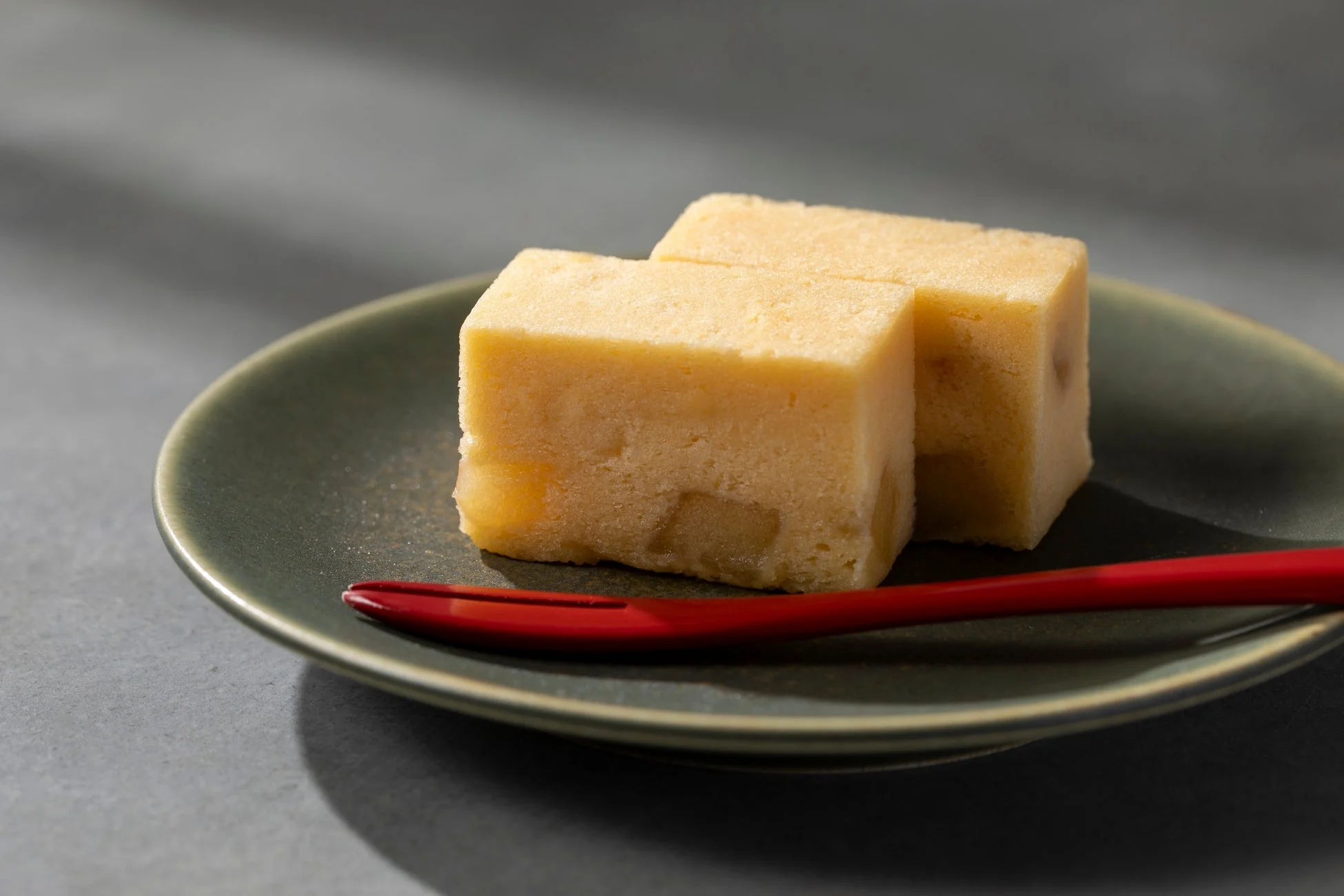 暗い緑色の皿に、淡い黄色で四角い形をしたお菓子が2つ置かれています