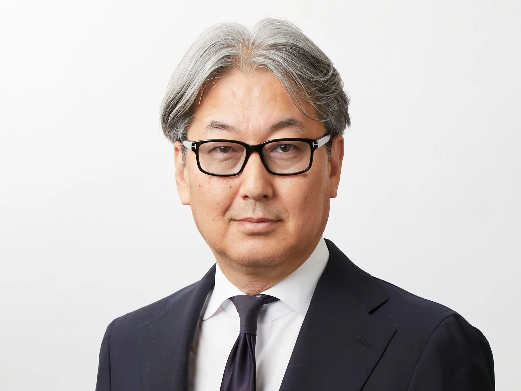 眼鏡をかけたグレイヘアのアジア人男性が、ダークスーツとネクタイを着用し、カメラをまっすぐ見つめているビジネスポートレート。