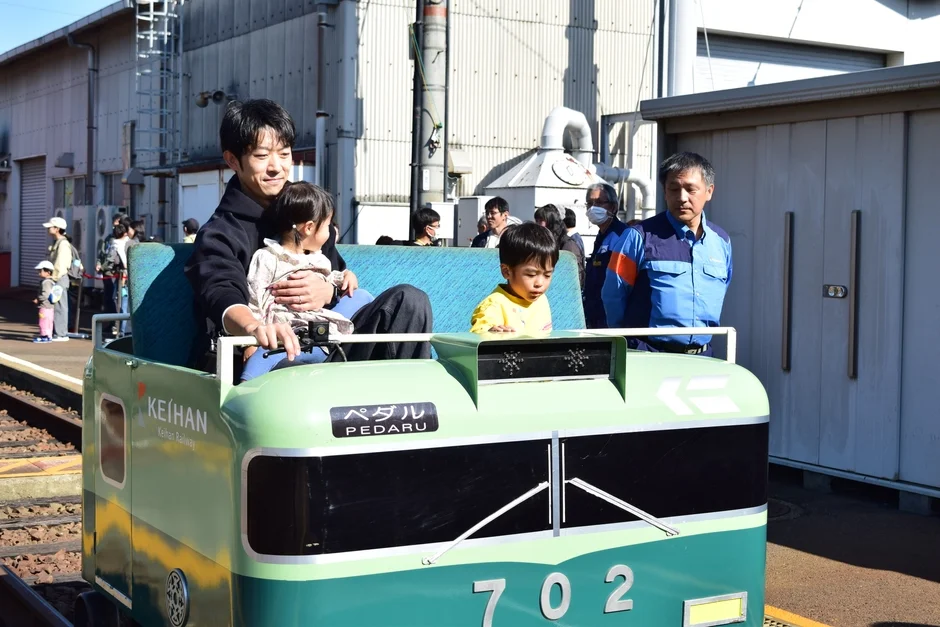 父親と2人の子供が、京阪電車のペダル列車に乗って楽しんでいる様子