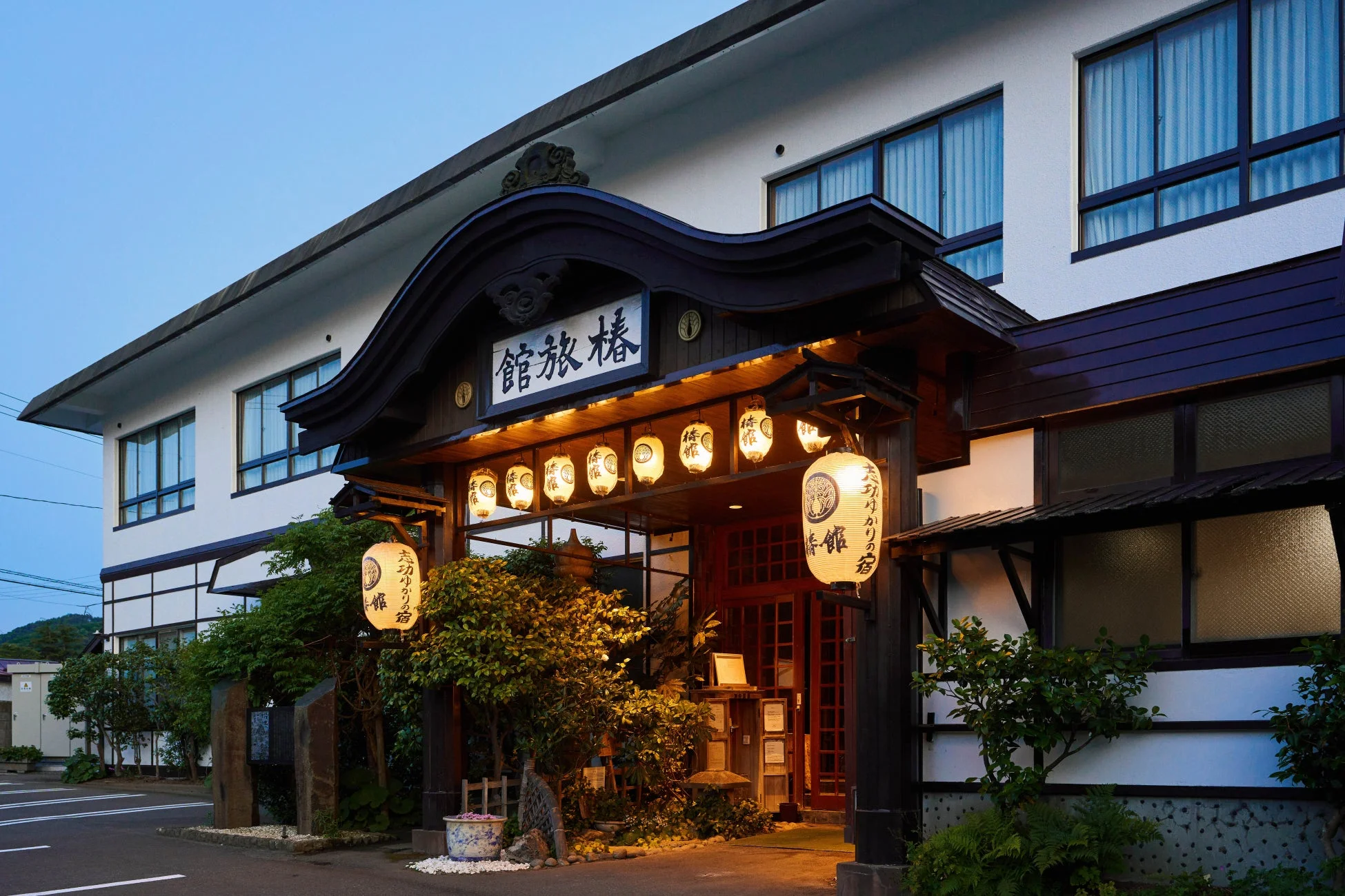 夕暮れ時に温かい光を放つ提灯が特徴的な椿旅館のエントランス